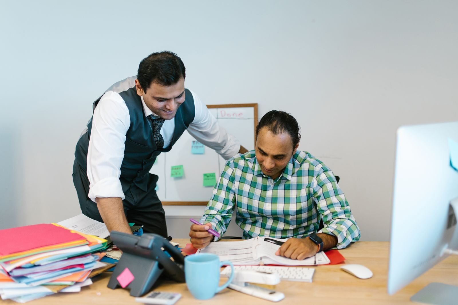 Two professional men collaborating in an office environment, reviewing documents and discussing strategies.