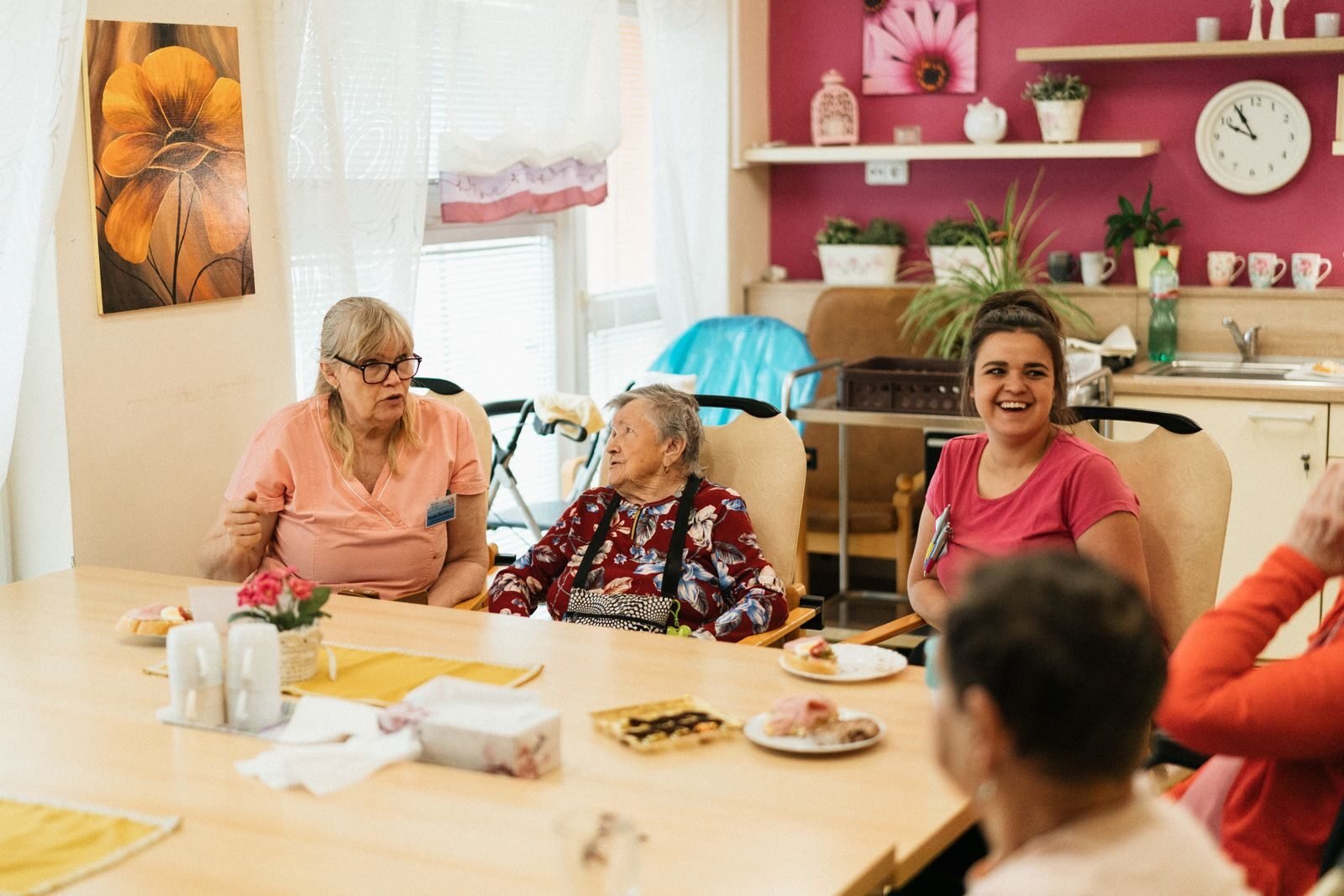 Elderly residents and caregivers enjoying a meal and conversation in a cheerful dining space.